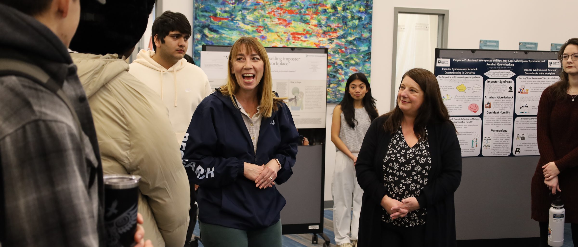 A TRU faculty member laughs with students at an undergraduate research showcase, surrounded by research posters.