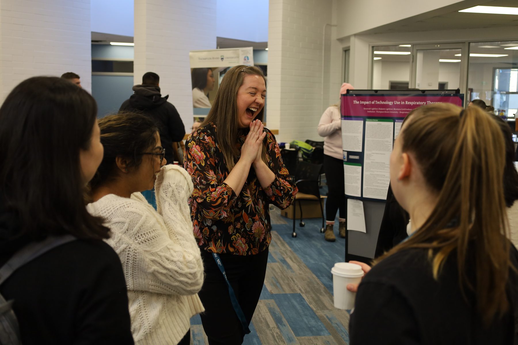 A faculty mentor shares a laugh with a small group of students at a research poster session.