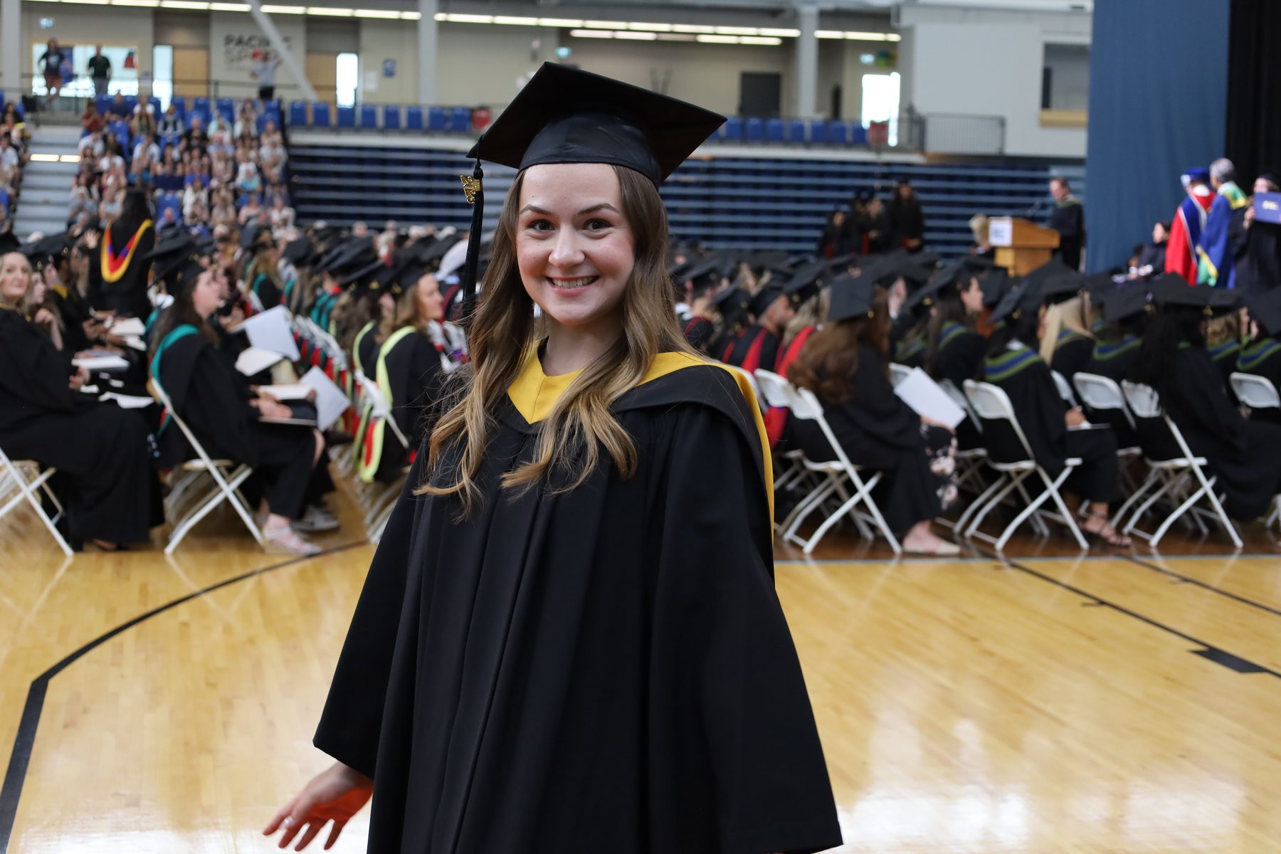 A TRU graduate smiles in cap and gown at convocation.